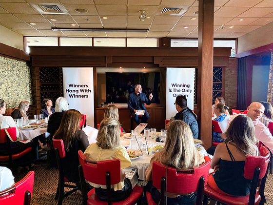 Networking lunch with seated attendees in a restaurant-like room, with presentation screens at the front.