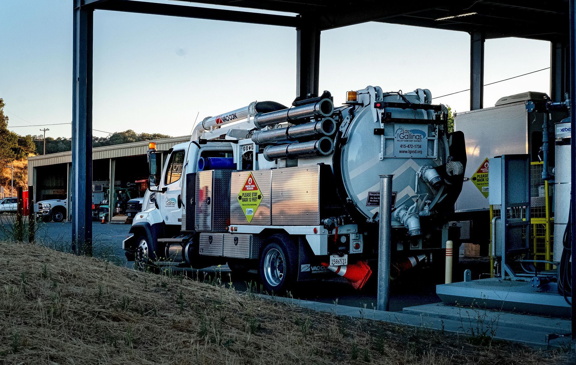 A vacuum truck is parked under a roof in a parking lot.