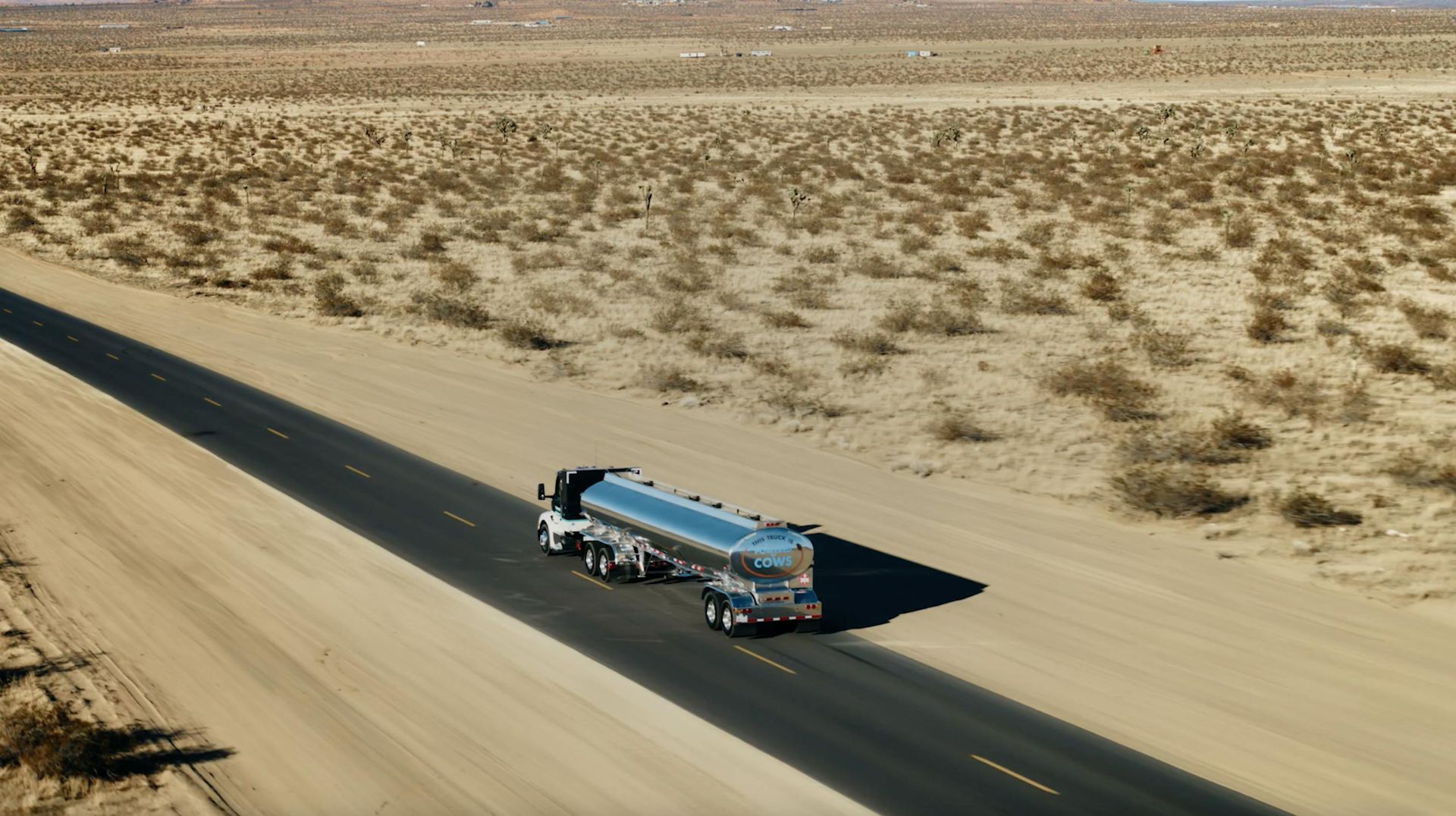 An aerial view of a tanker truck driving down a dirt road in the desert.