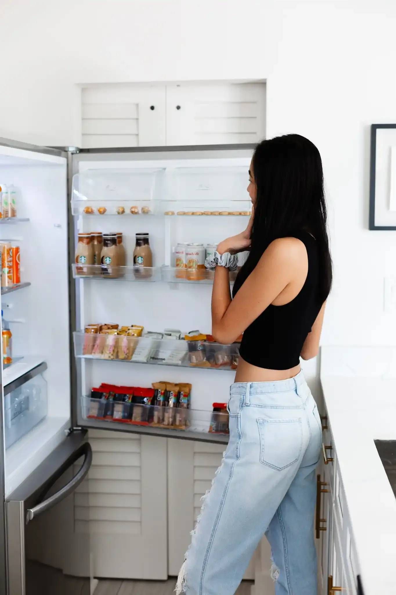 A woman is standing in front of an open refrigerator in a kitchen.