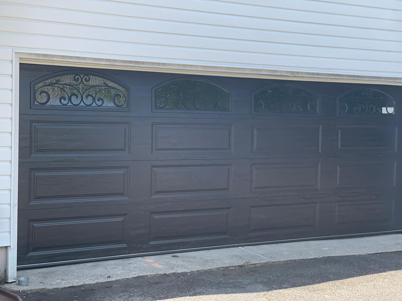 A black garage door is sitting in front of a white house – New Jersey - Local Garage Door