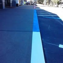 Blue painted concrete, with a light blue stripe separating darker concrete on the left and black asphalt on the right.