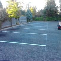 Empty asphalt parking lot with white painted lines and a small vehicle.