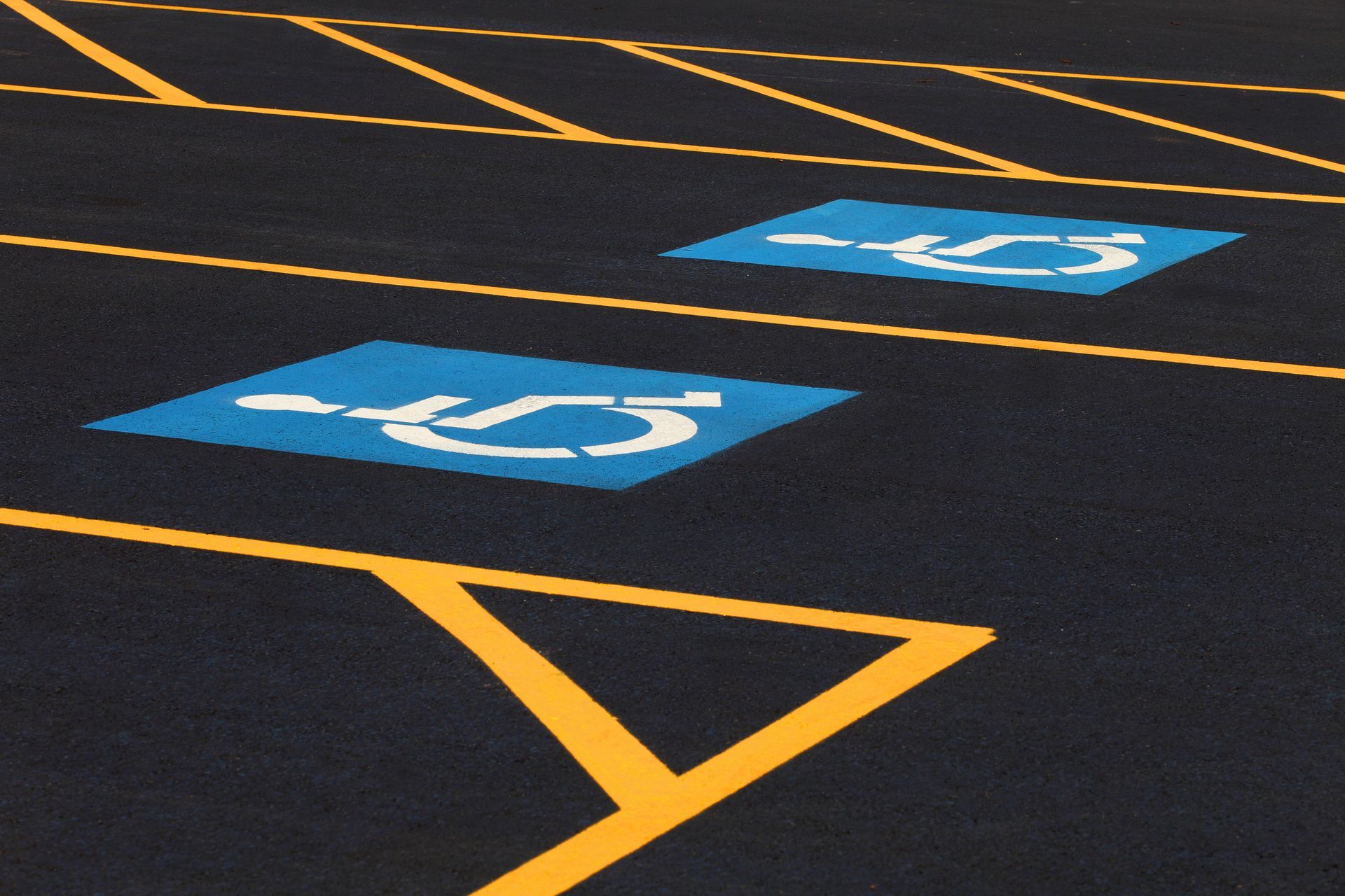 Two blue handicap parking spaces with white wheelchair symbols, on black asphalt with yellow parking lines.