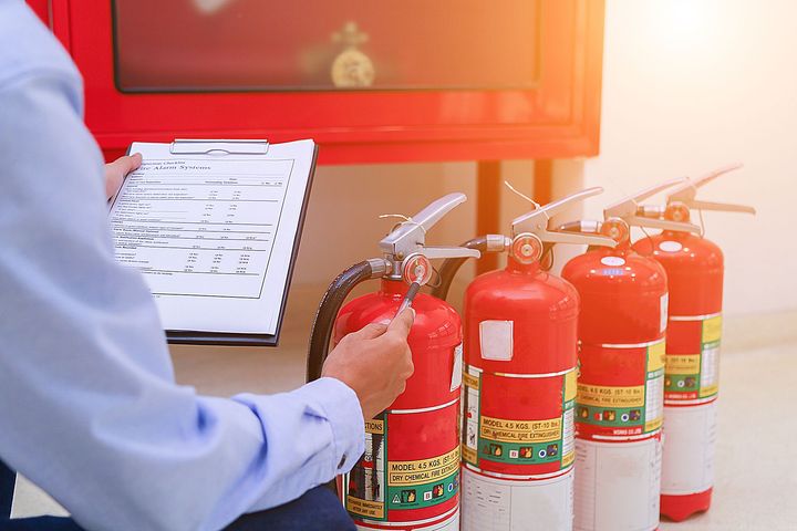 A man is sitting in front of a row of fire extinguishers.