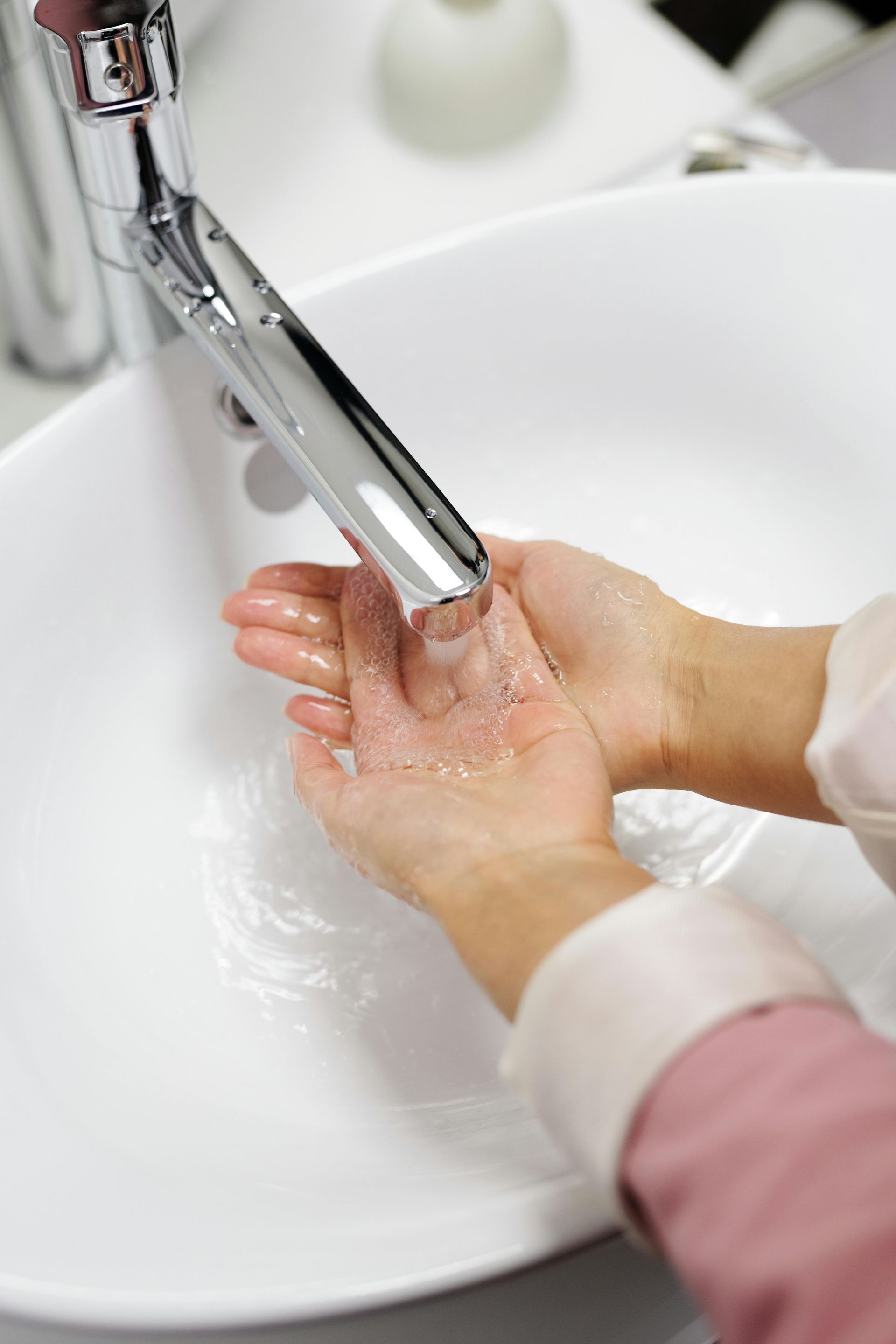 Hands catching running tap water in a bathroom sink as part of plumbing services in Little Canford.