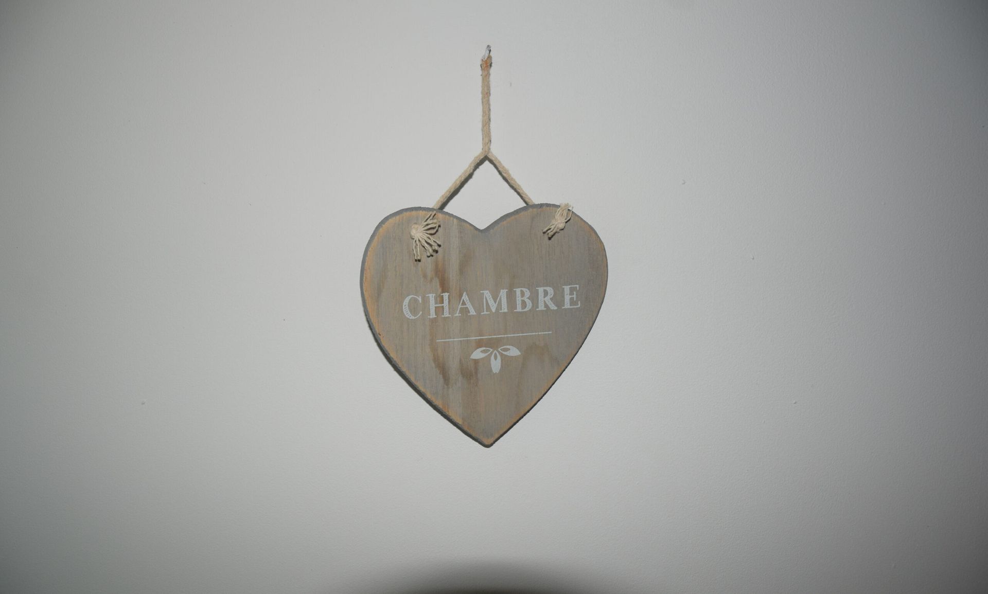 Un panneau en forme de coeur en bois accroché sur un mur blanc.