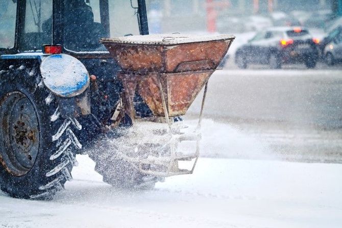 Tractor spreading salt or sand on a snowy road in heavy snowfall