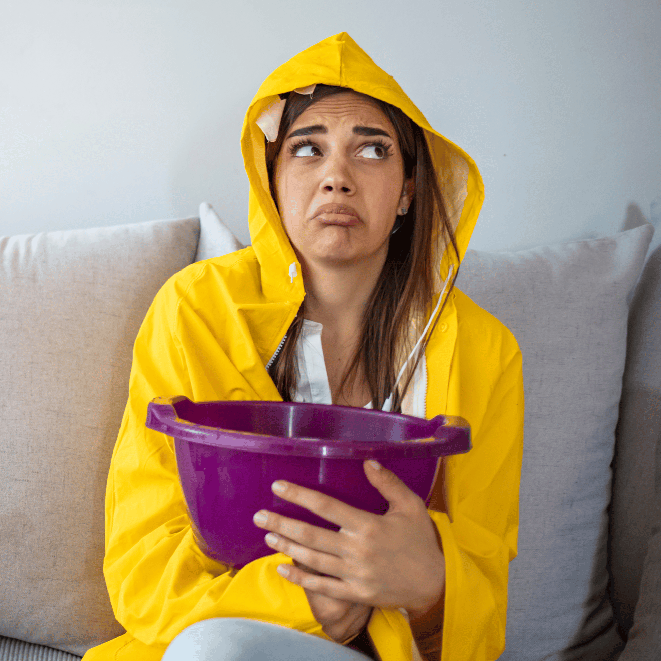 A woman in a yellow raincoat is sitting on a couch holding a purple bowl.