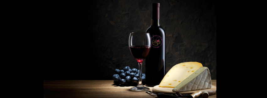 A bottle of wine , a glass of wine , a piece of cheese and grapes on a table.