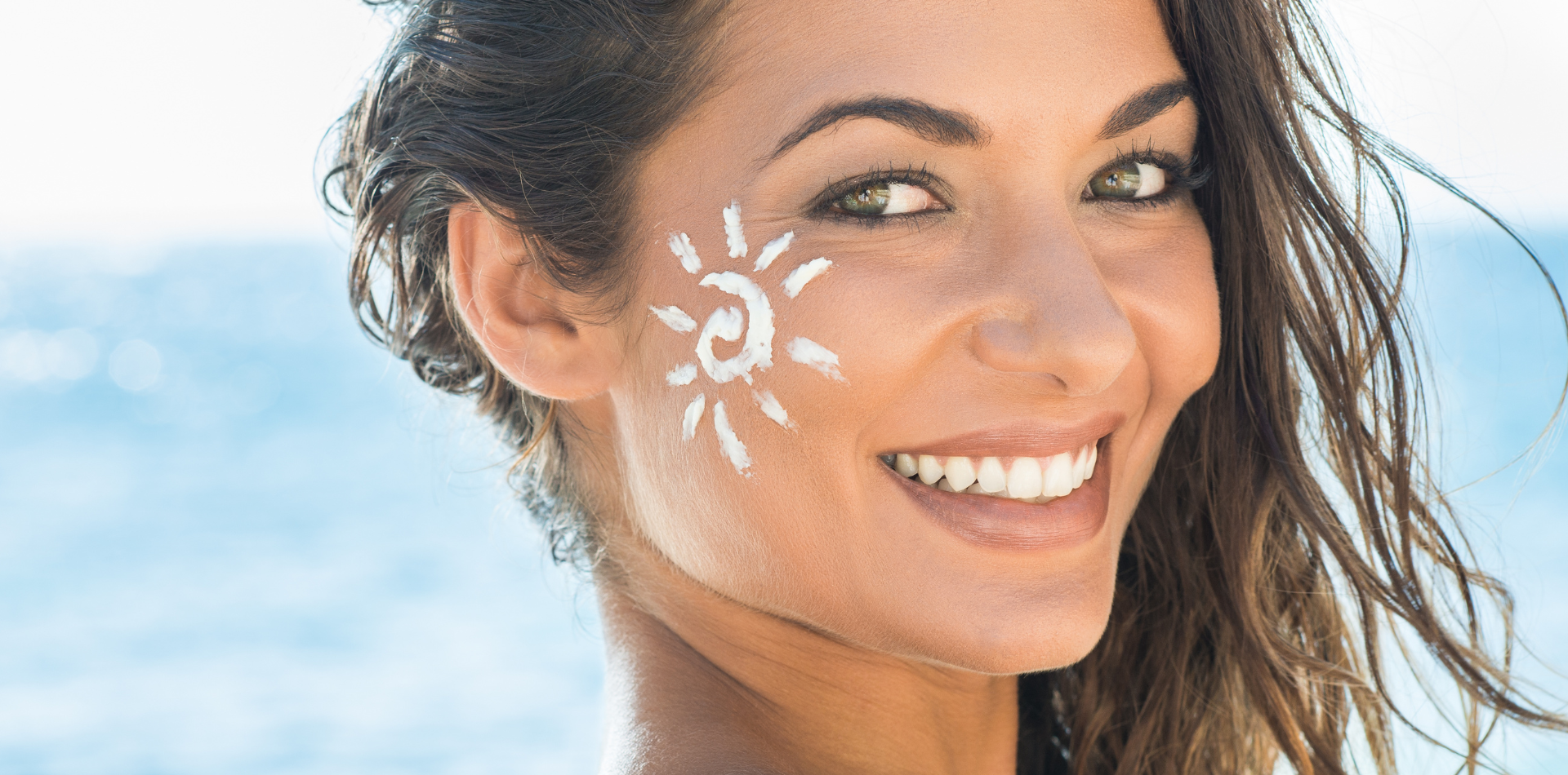 A woman is smiling with sunscreen on her face.