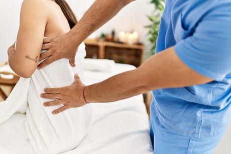Therapist giving a back massage to a person wrapped in a towel, indoors.