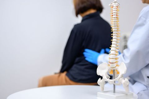 Doctor examining a patient's back; a spine model sits on a table in front.