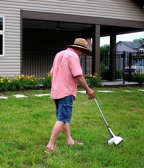 A man wearing a pink shirt and a hat is standing in the grass holding a metal detector.