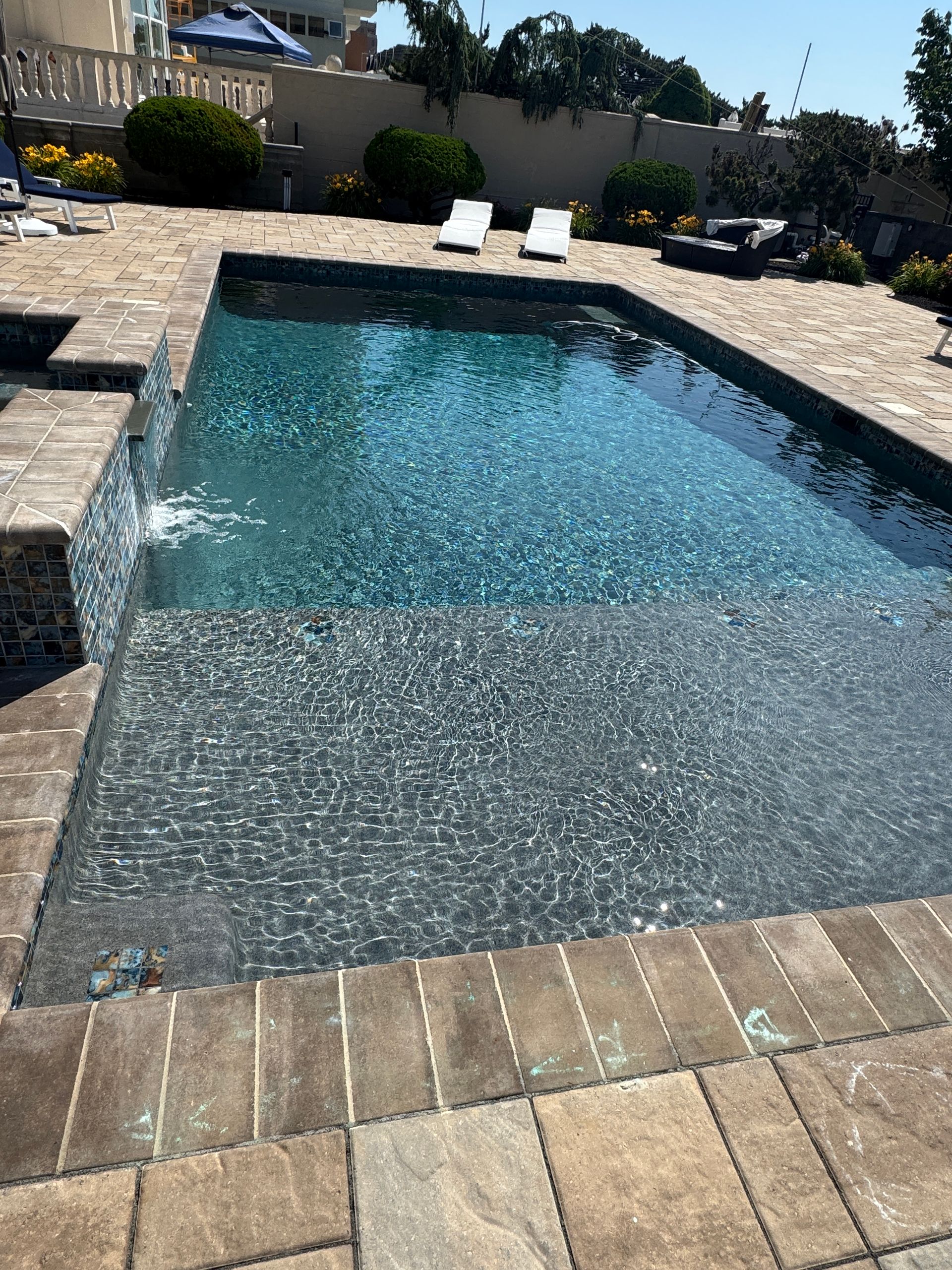 Backyard swimming pool with shimmering water and two white lounge chairs on a stone deck