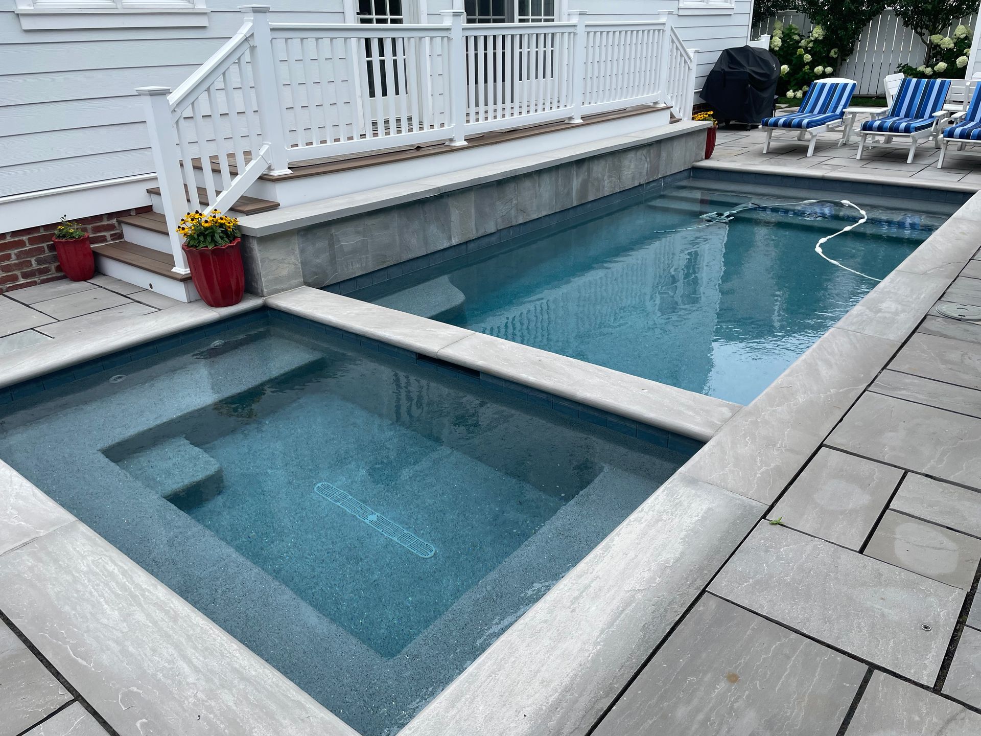 Backyard pool with a raised hot tub, blue lounge chairs, and white deck railing
