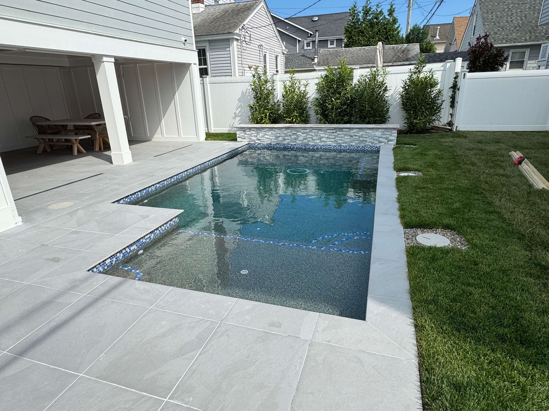 Modern backyard with a rectangular pool, white patio, and green lawn beside a house