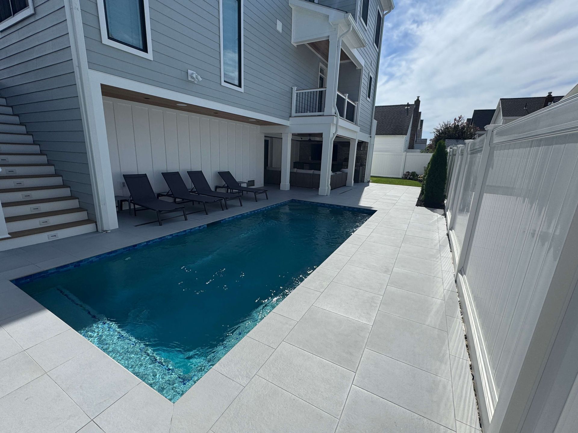 Backyard pool beside a gray house, with lounge chairs and a white fence along the deck.
