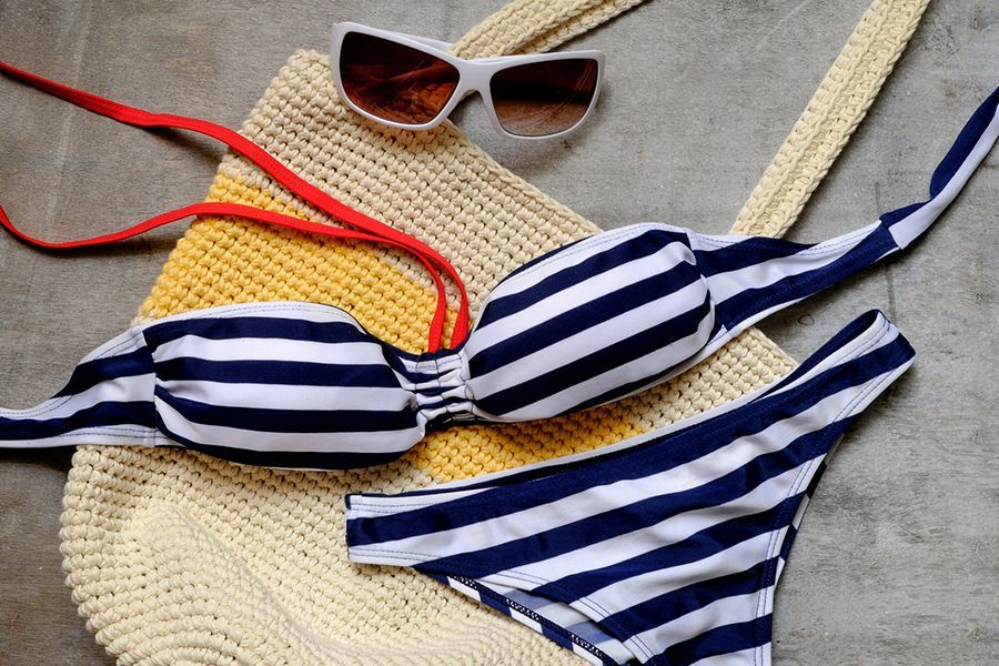 Bikini a righe blu e bianche con occhiali da sole e borsa da spiaggia intrecciata.