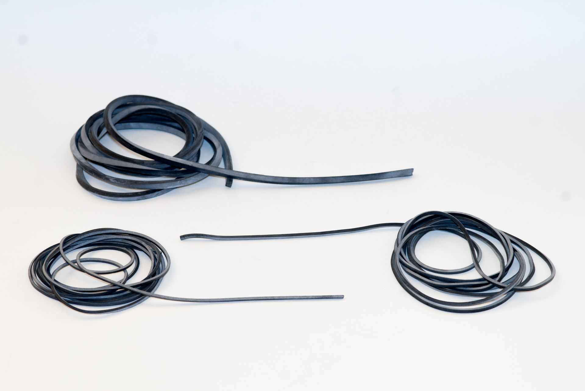 Mucchio aggrovigliato di sottili strisce di gomma nera su uno sfondo bianco.