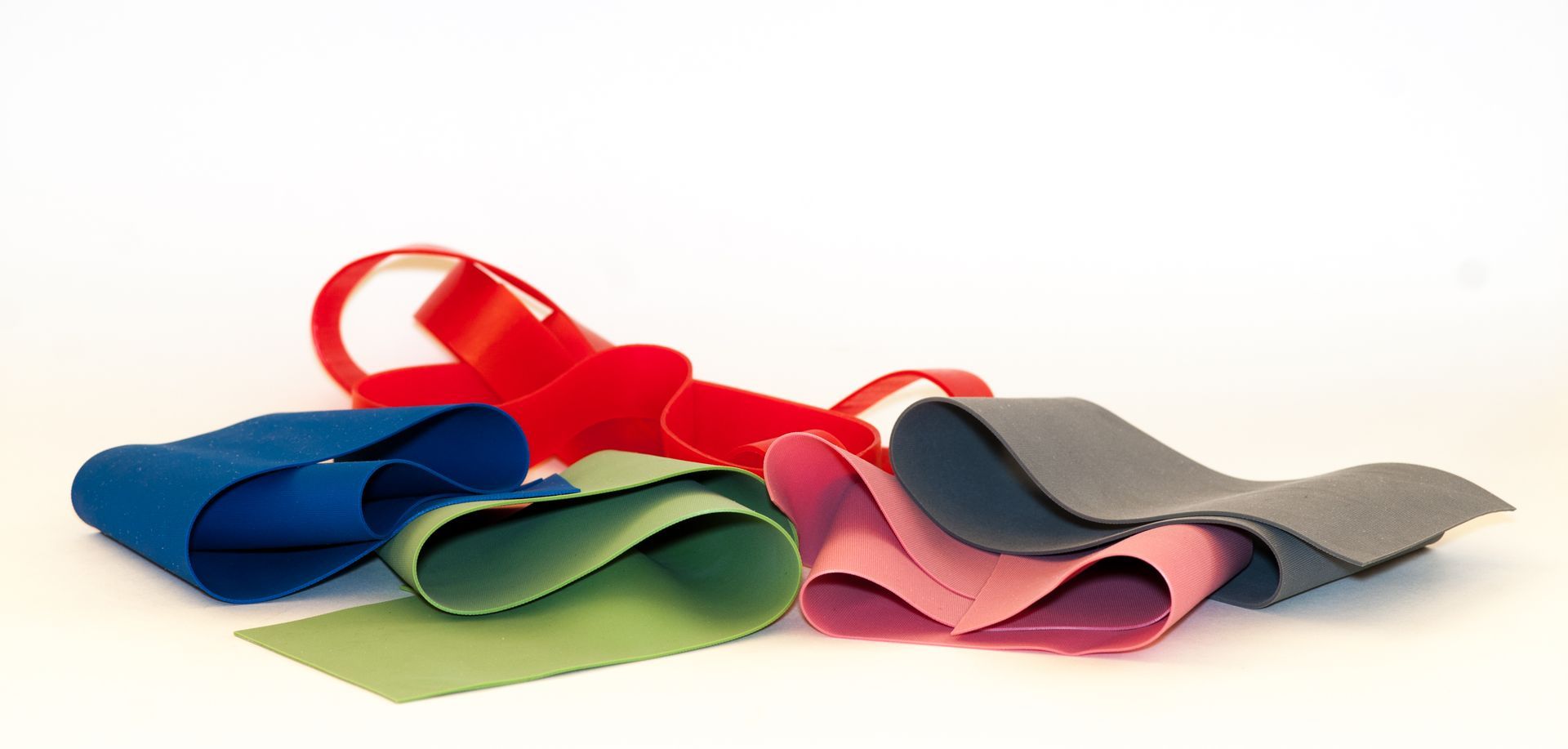 Fasce elastiche colorate, attorcigliate e arrotolate insieme su una superficie bianca.