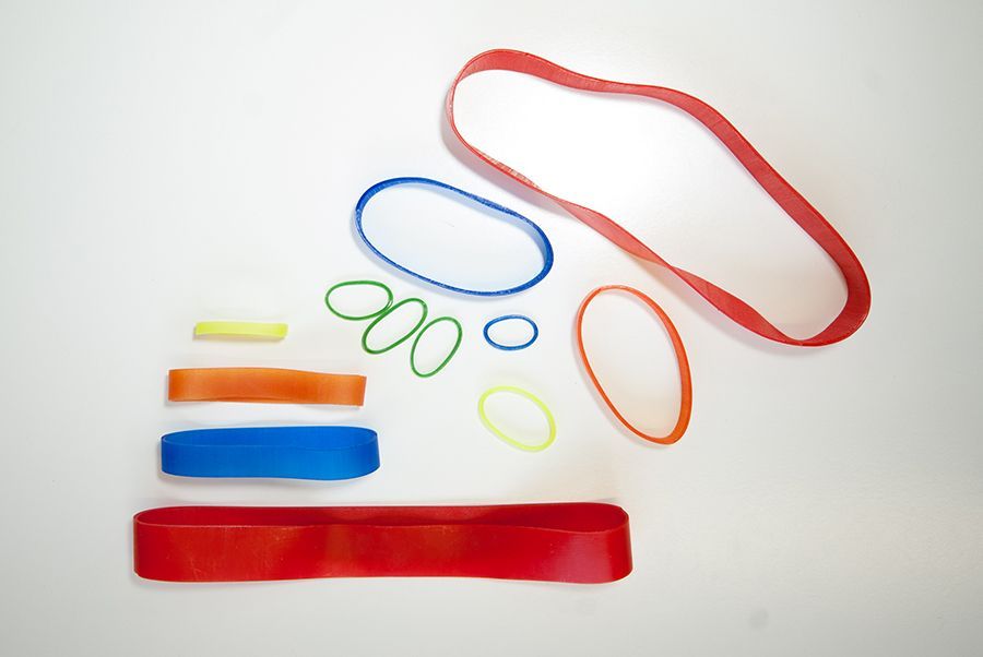 Una collezione di elastici colorati di varie dimensioni e forme, su una superficie bianca.