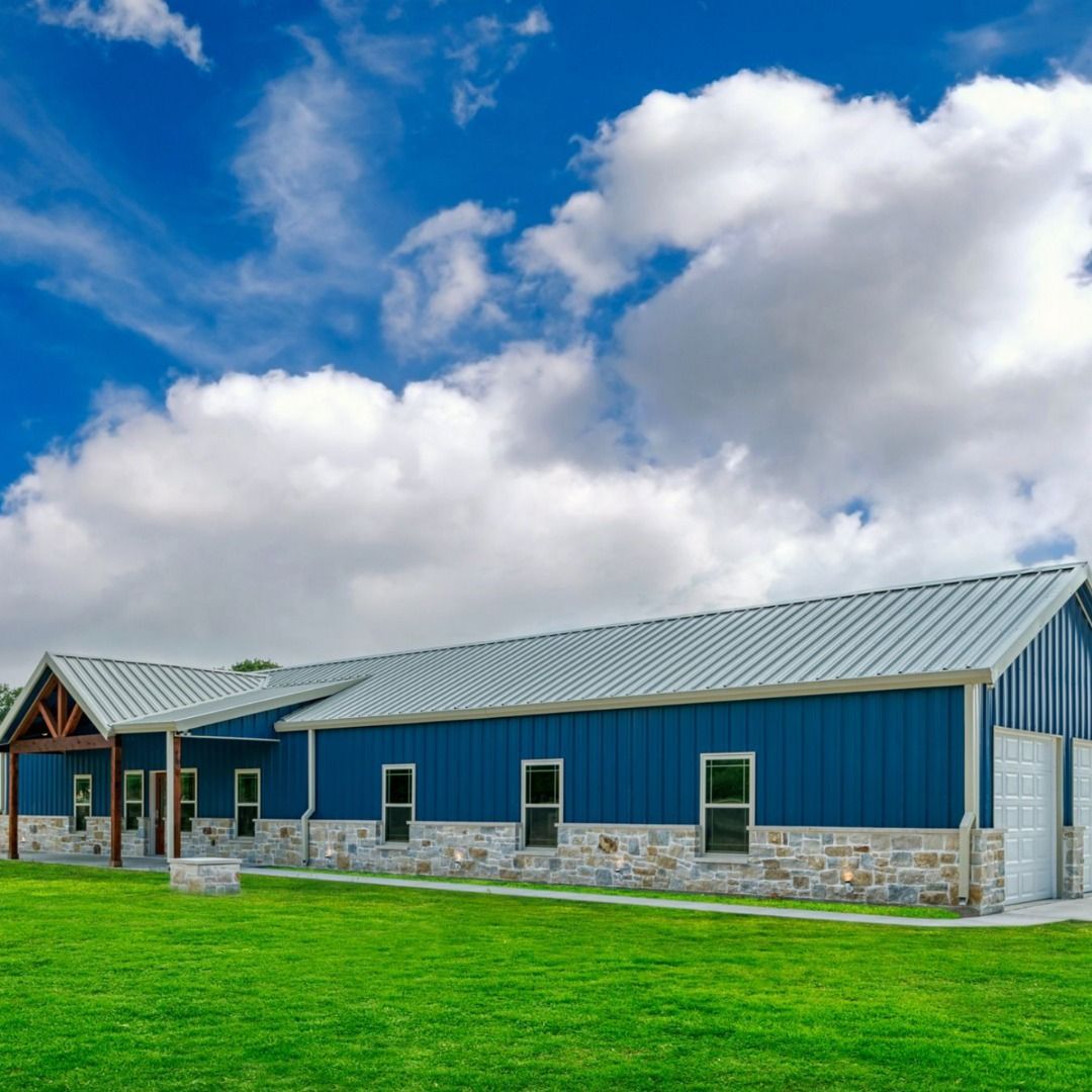 A blue house with a metal roof is sitting on top of a lush green field.