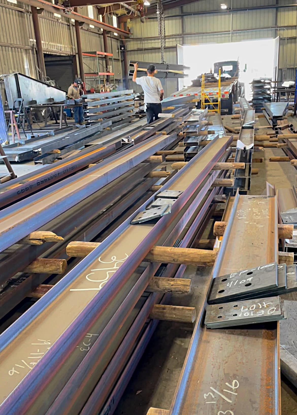 A man is standing on a row of metal beams in a factory.