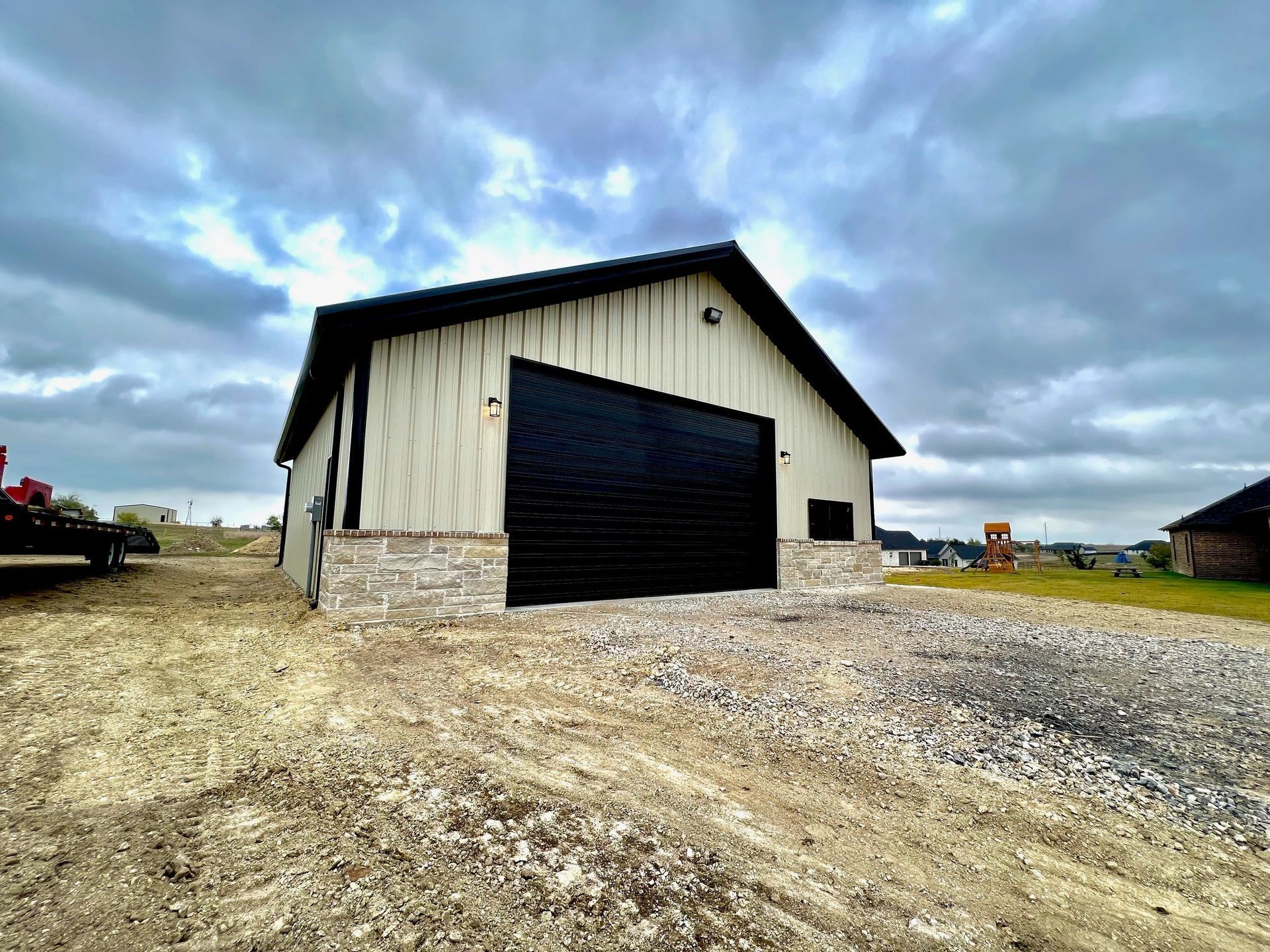 A garage with a black garage door is sitting in the middle of a dirt field.