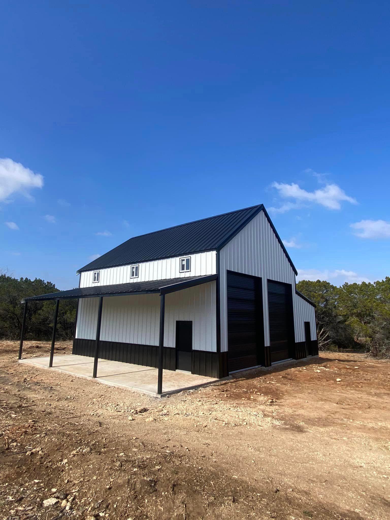 A white and black barn is sitting in the middle of a dirt field.