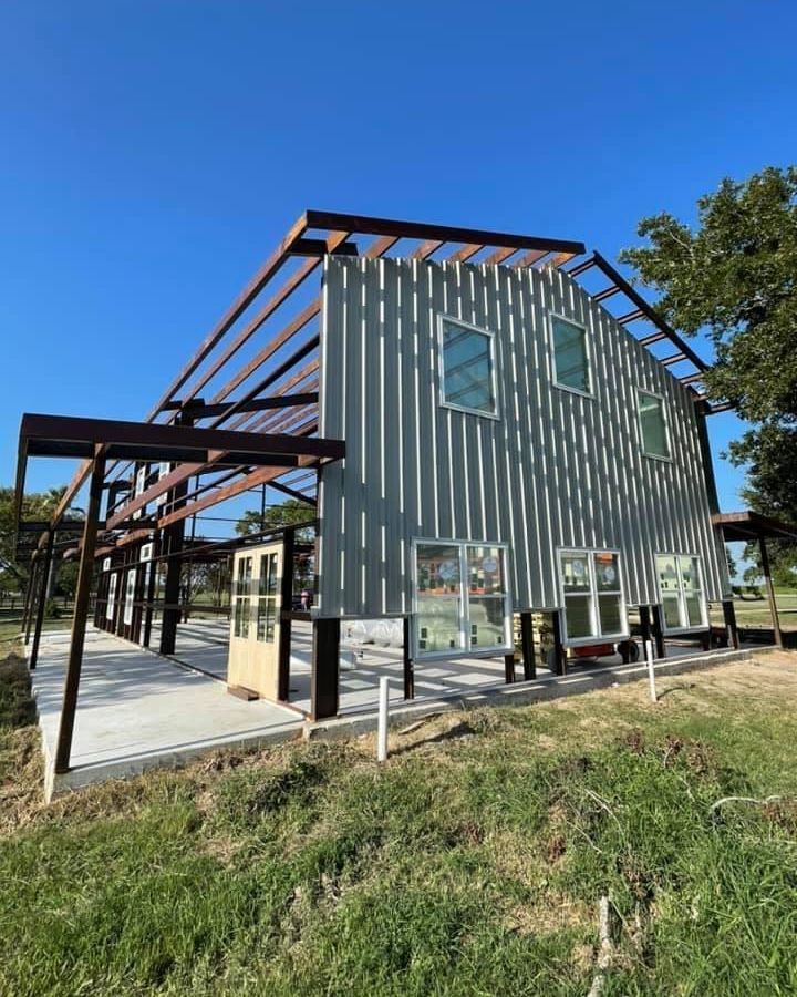 A large metal building is being built in a grassy field.