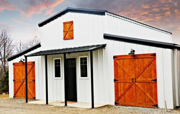 A white barn with two wooden garage doors and a porch.