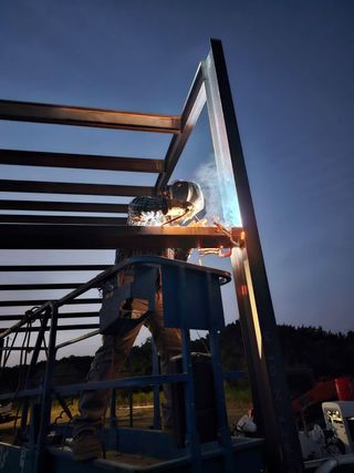 A man is welding a metal structure at night.