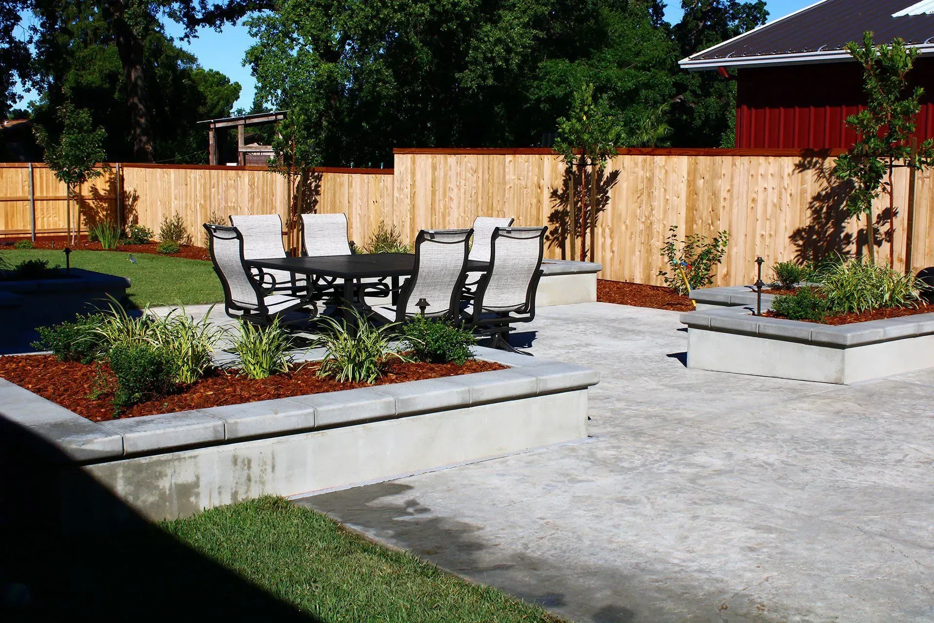 Patio with table, chairs, raised planters, and wooden fence. Sunny day.