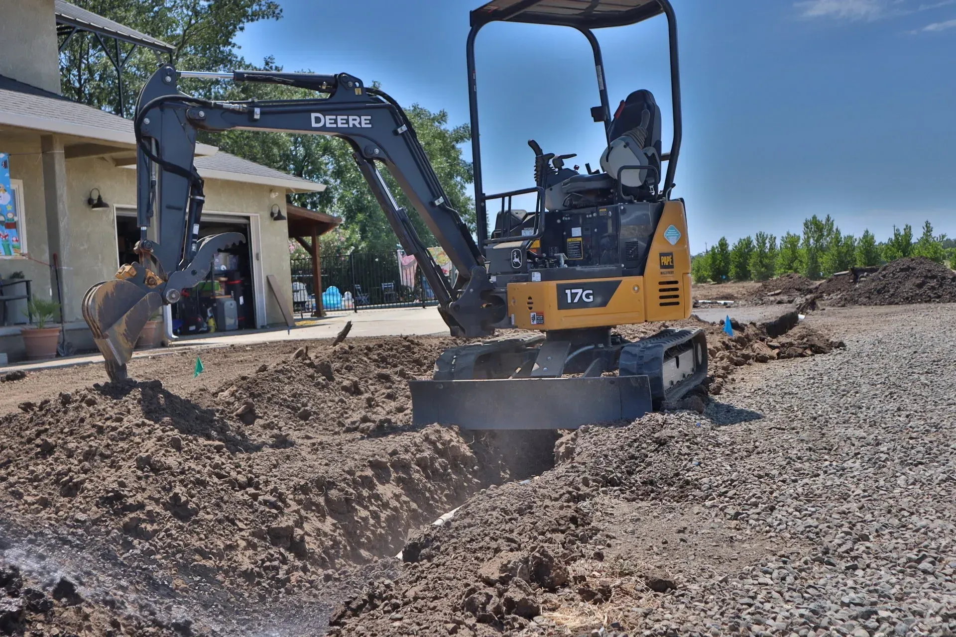 John Deere mini excavator digging a trench in a construction site with a building in the background.