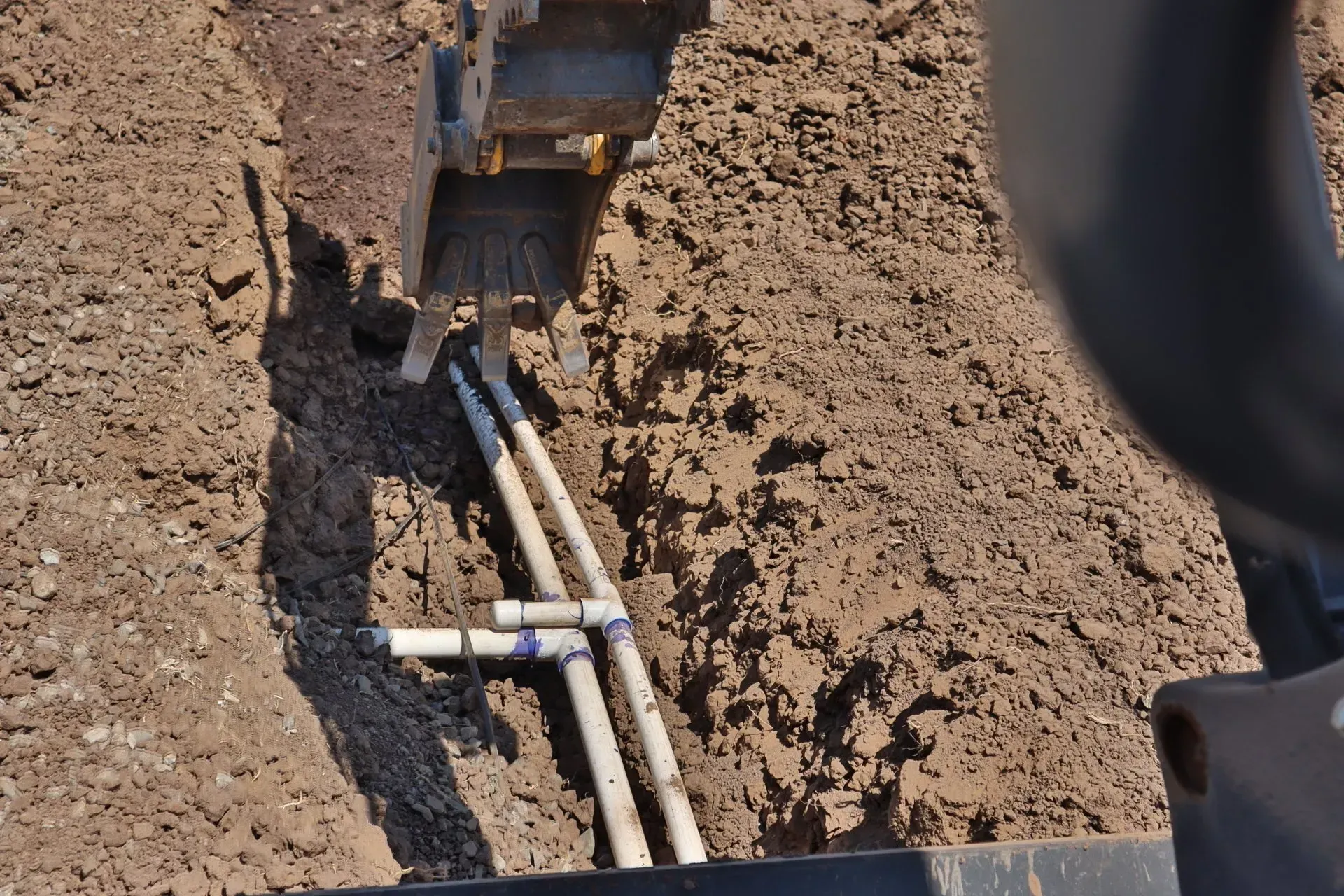 Pipes in trench, being worked on with heavy equipment, likely for construction or repairs.