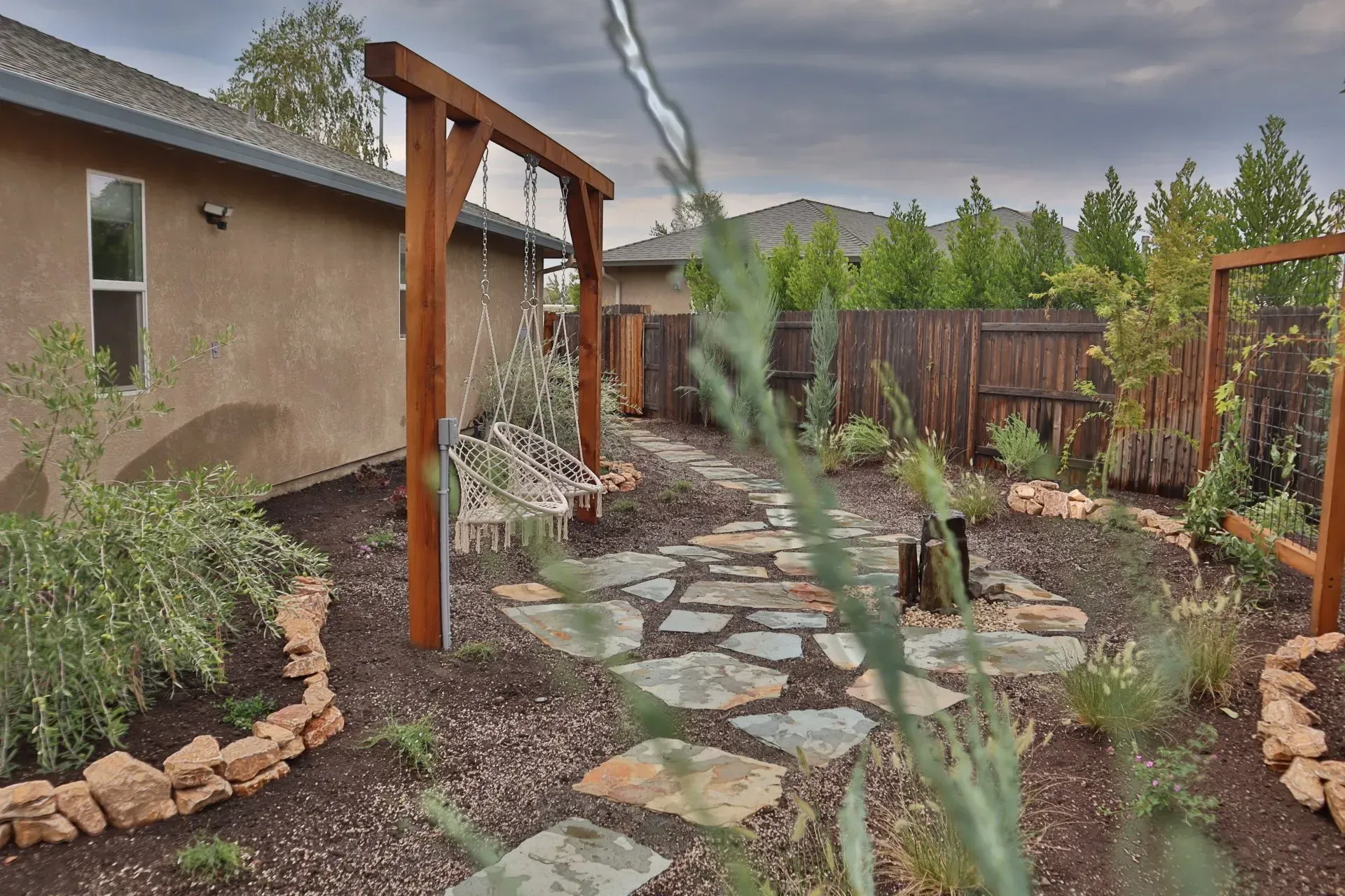 Yellow and gray soil compactor on gravel path; wooden structure in background.