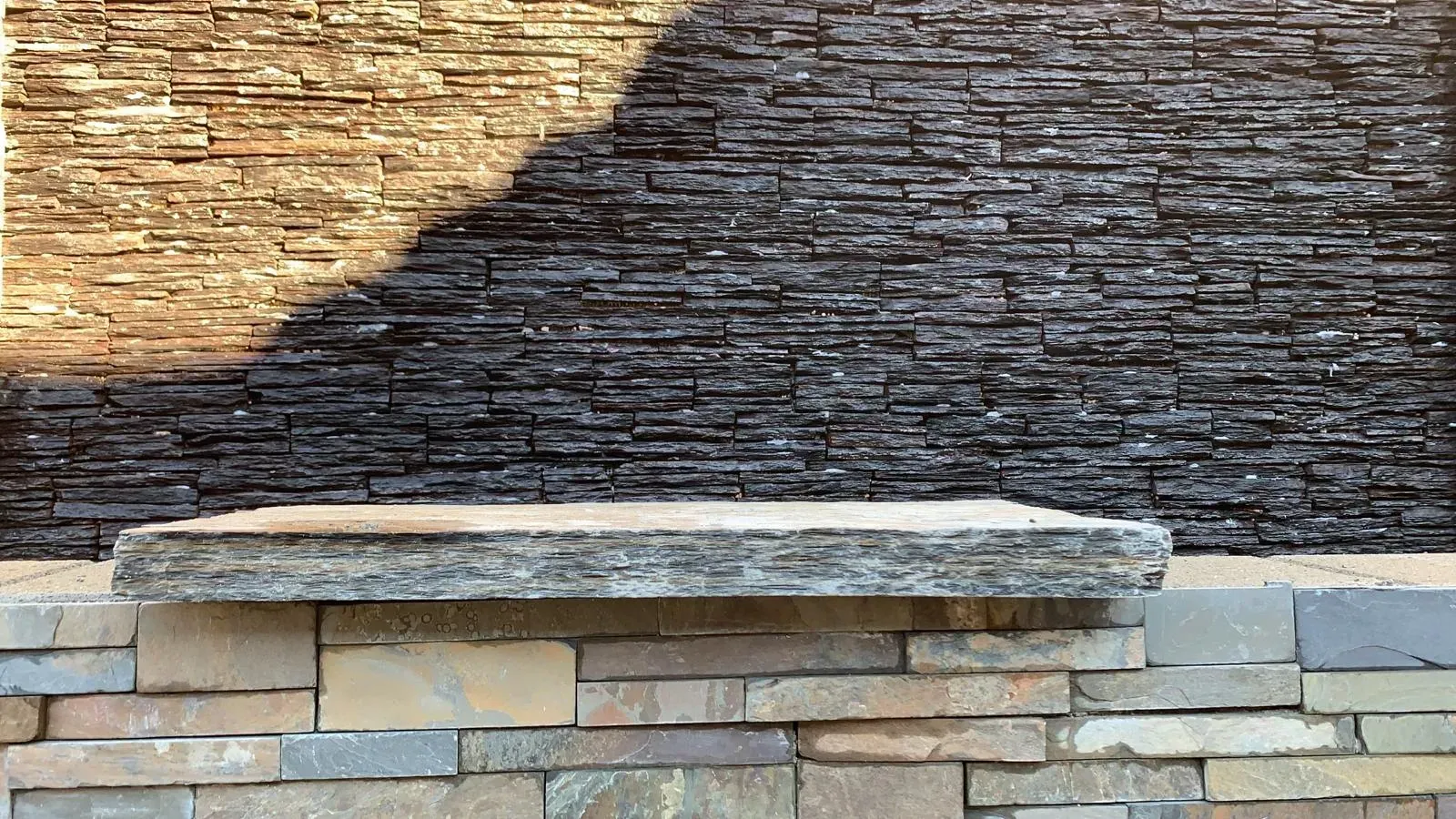 Stone bench in front of a layered stone wall, with light and shadow play.