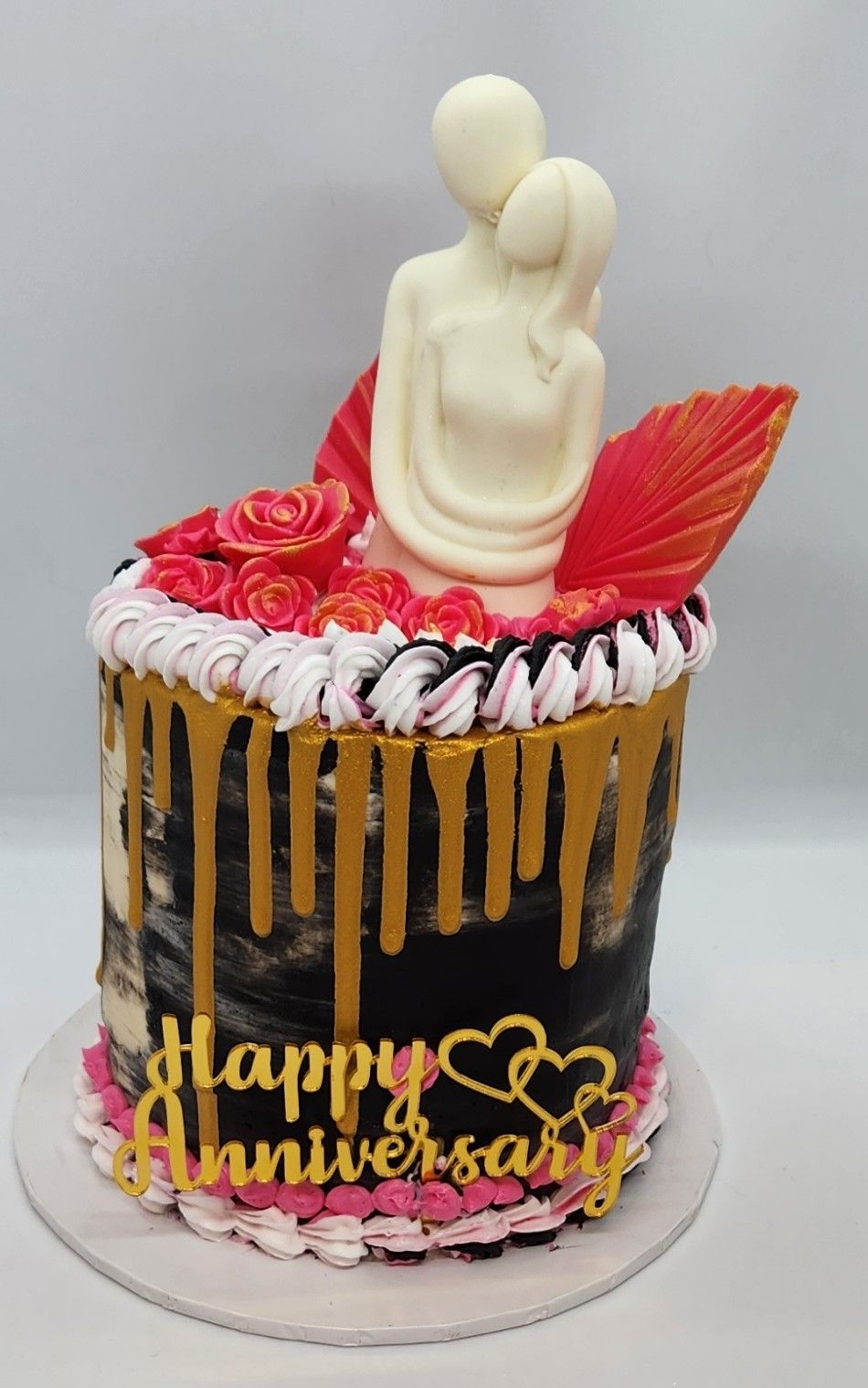 Anniversary cake with a white chocolate couple figurine, roses, gold drip, and 