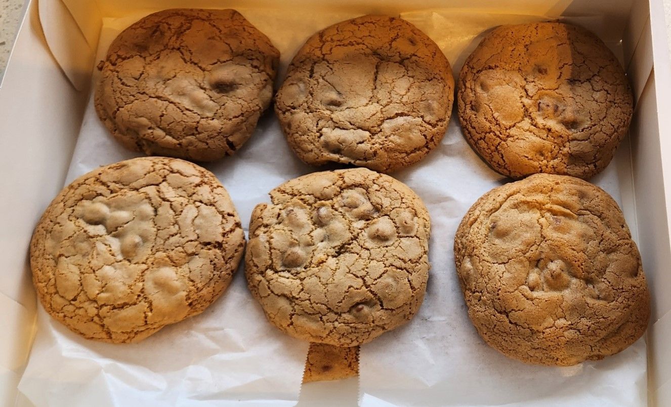 Six golden brown cookies in a box on white paper.