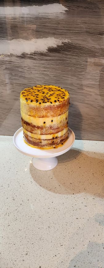 A multi-layered cake with passionfruit topping on a white pedestal, against a wooden background.