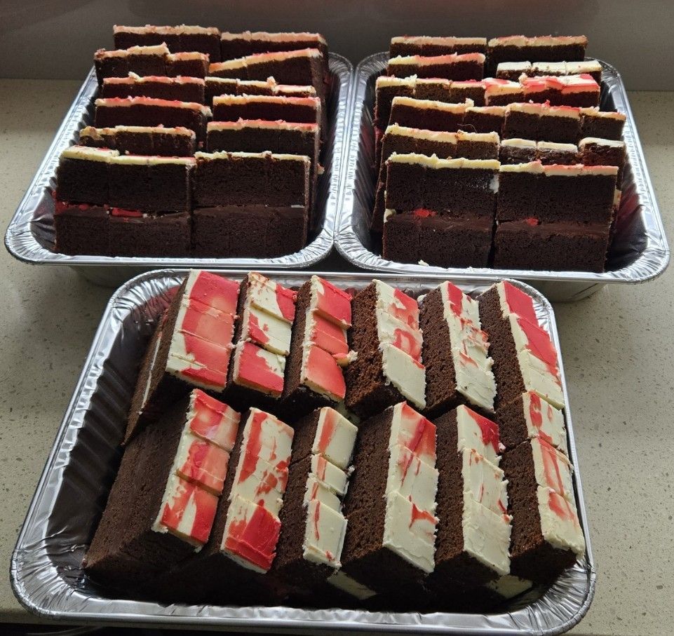 Three foil trays filled with sliced chocolate cakes, various frosting colors.