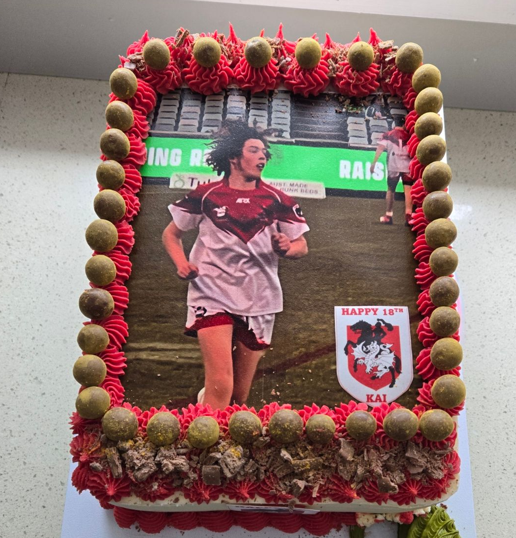 Cake with a photo of a rugby player. Red and gold decorations surround the image, along with a team crest.