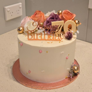 White frosted cake decorated with flowers, gold accents, and 