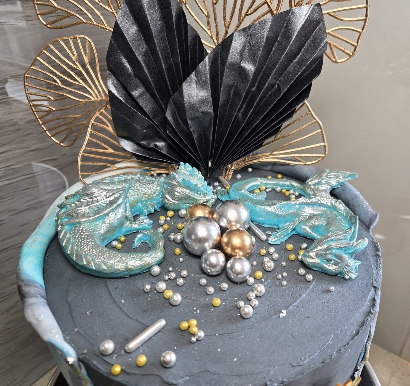 Gray cake with teal and silver dragon decorations and gold and black accents.