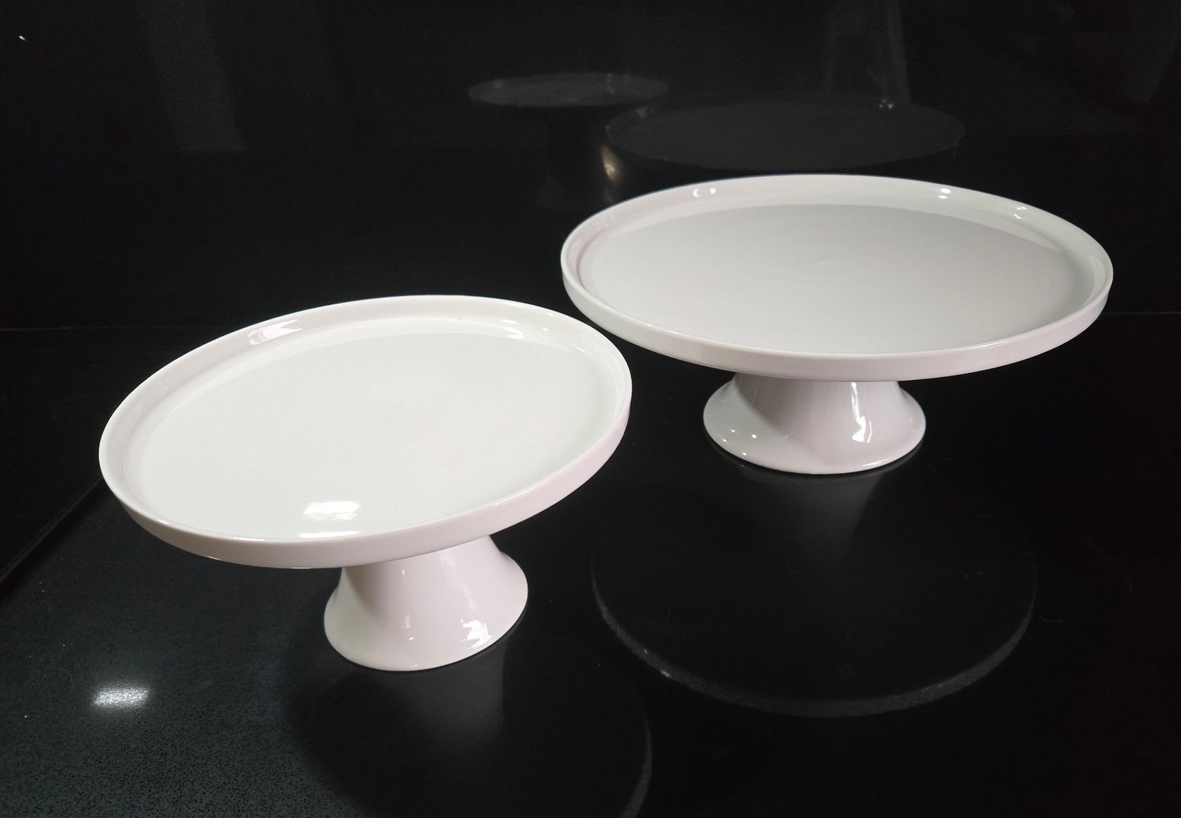 Two white ceramic cake stands on a reflective black surface.