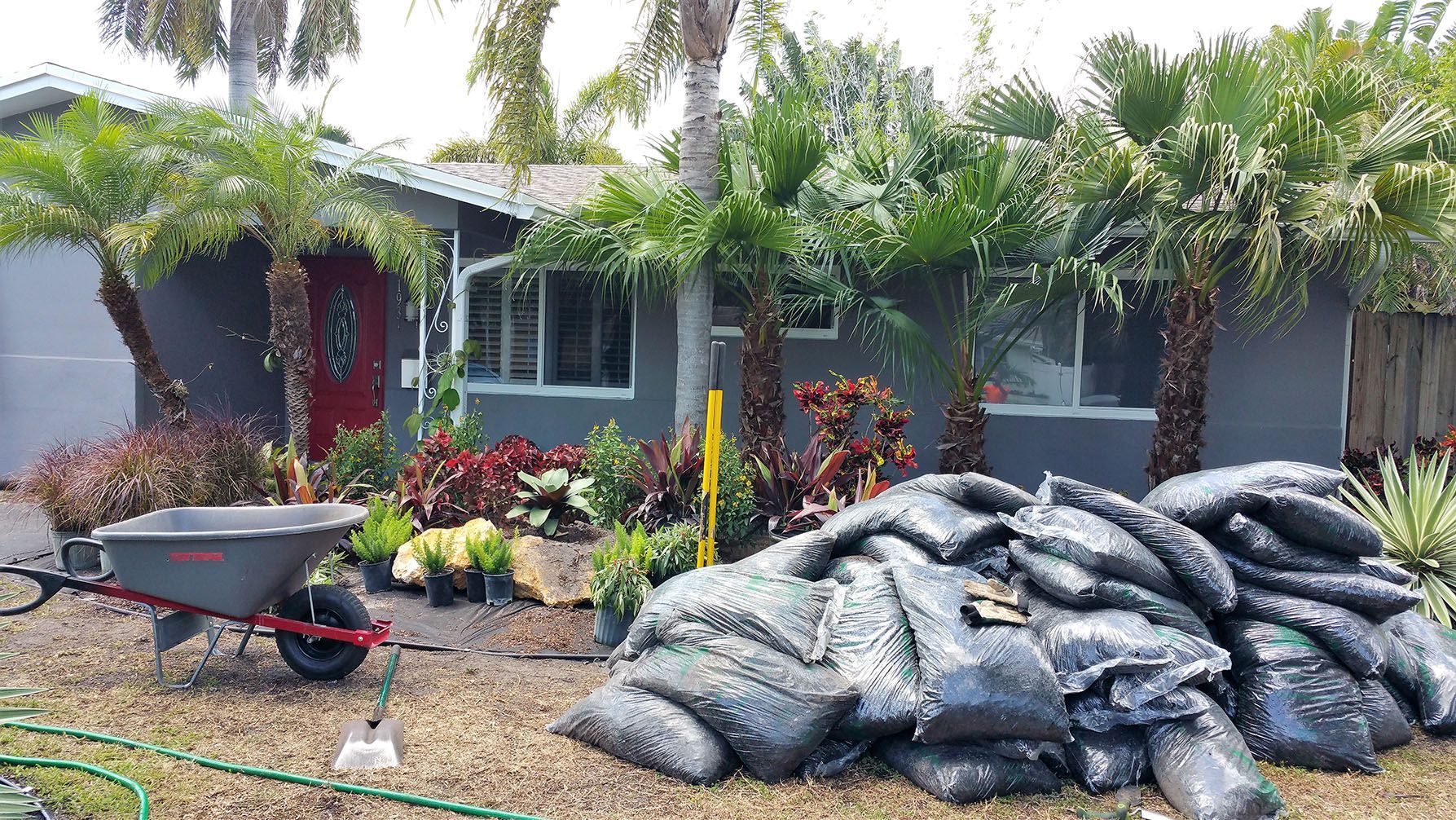 A wheelbarrow is parked in front of a house next to a pile of bags.