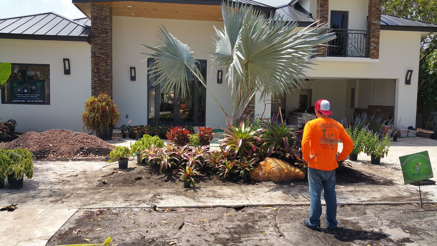A man in an orange shirt is standing in front of a house.