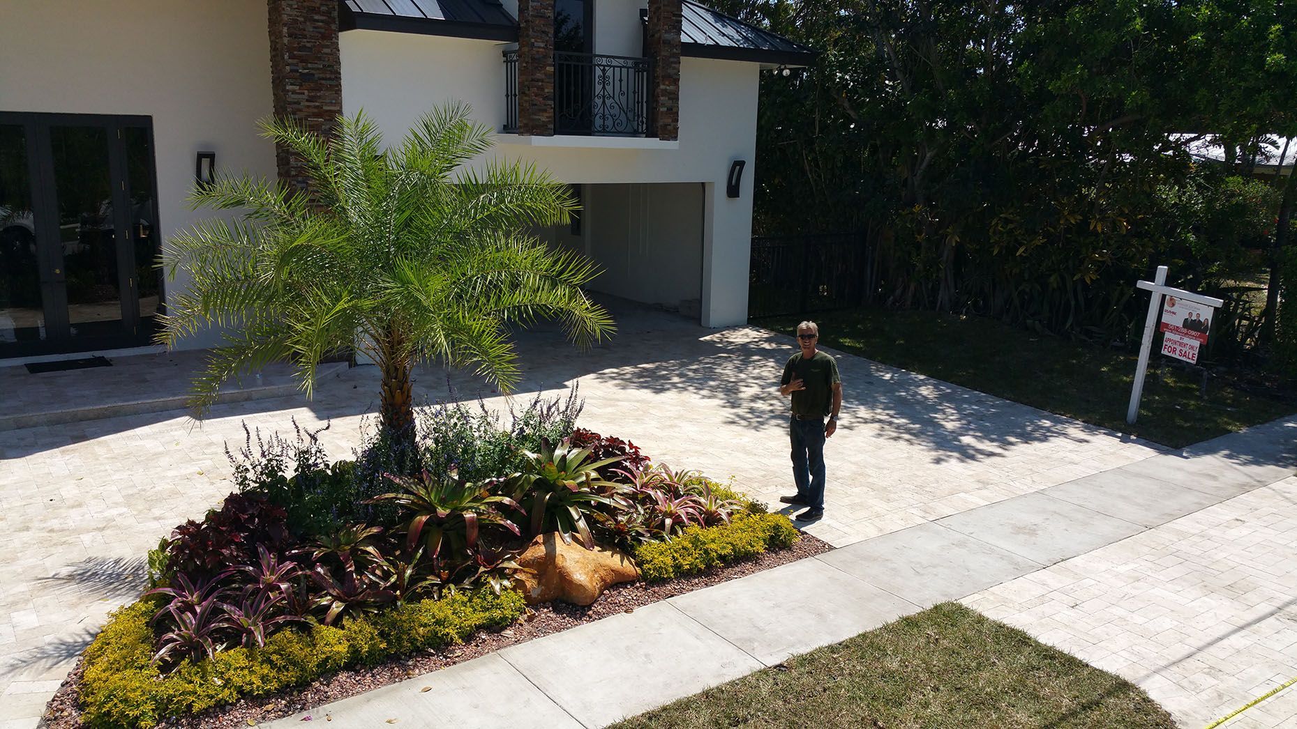 A man is standing in front of a house with a for sale sign in the background.