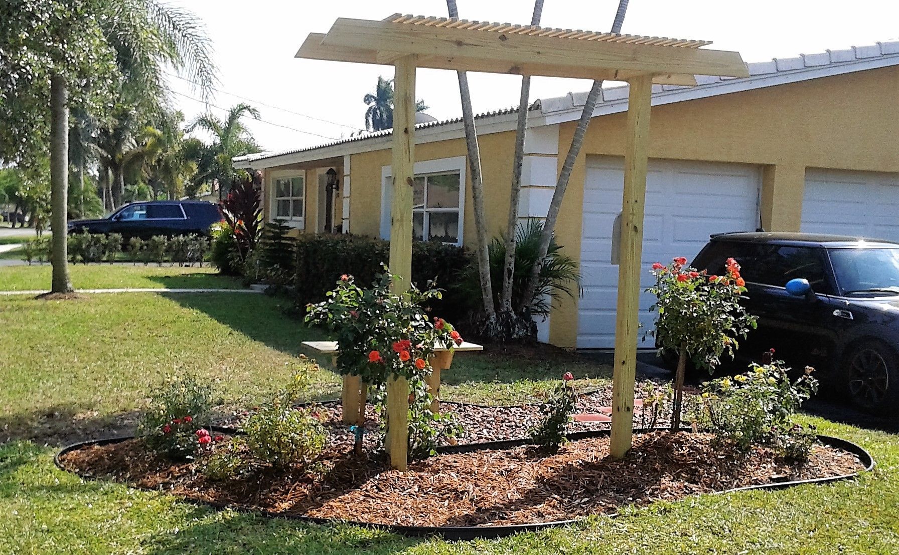 A car is parked in front of a house with a wooden pergola.